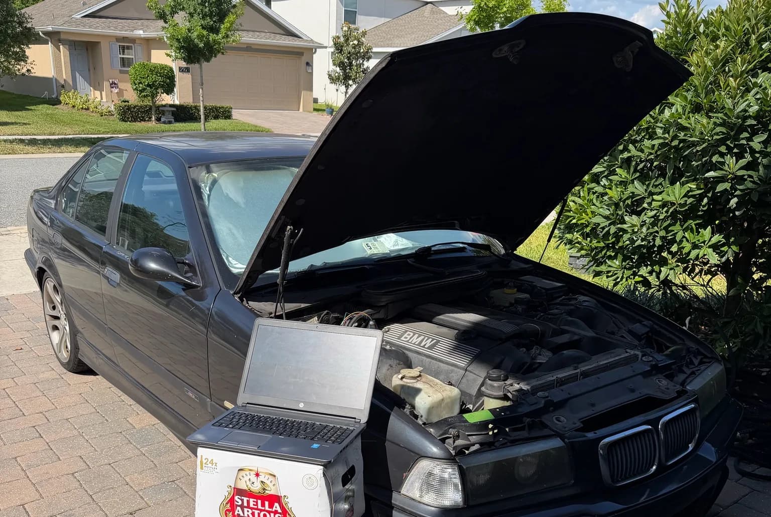 A laptop running diagnostics on an E36 BMW in a Florida driveway
