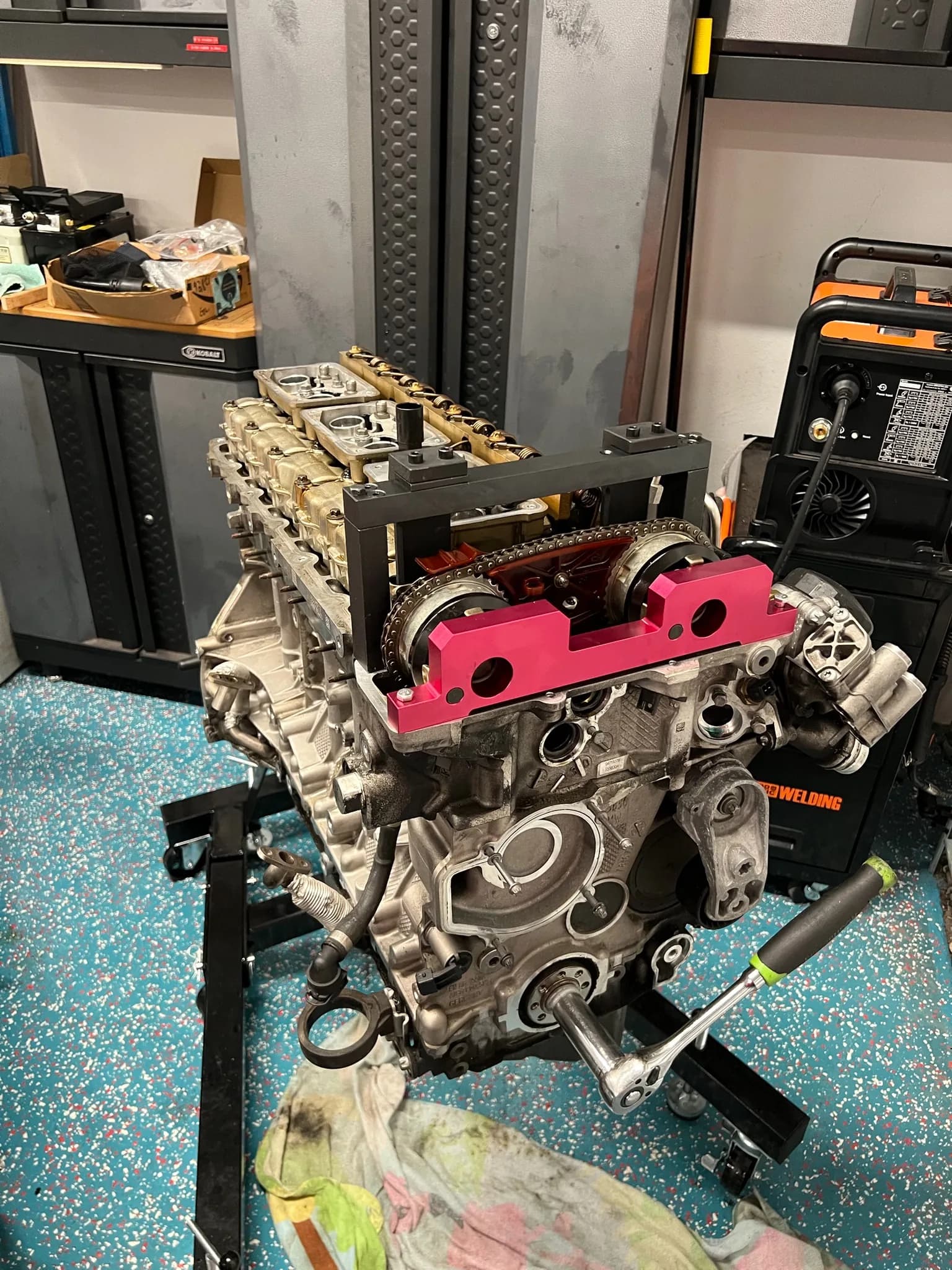 A stripped BMW S55 inline-six on an engine stand with cam-timing tools clamped to the head