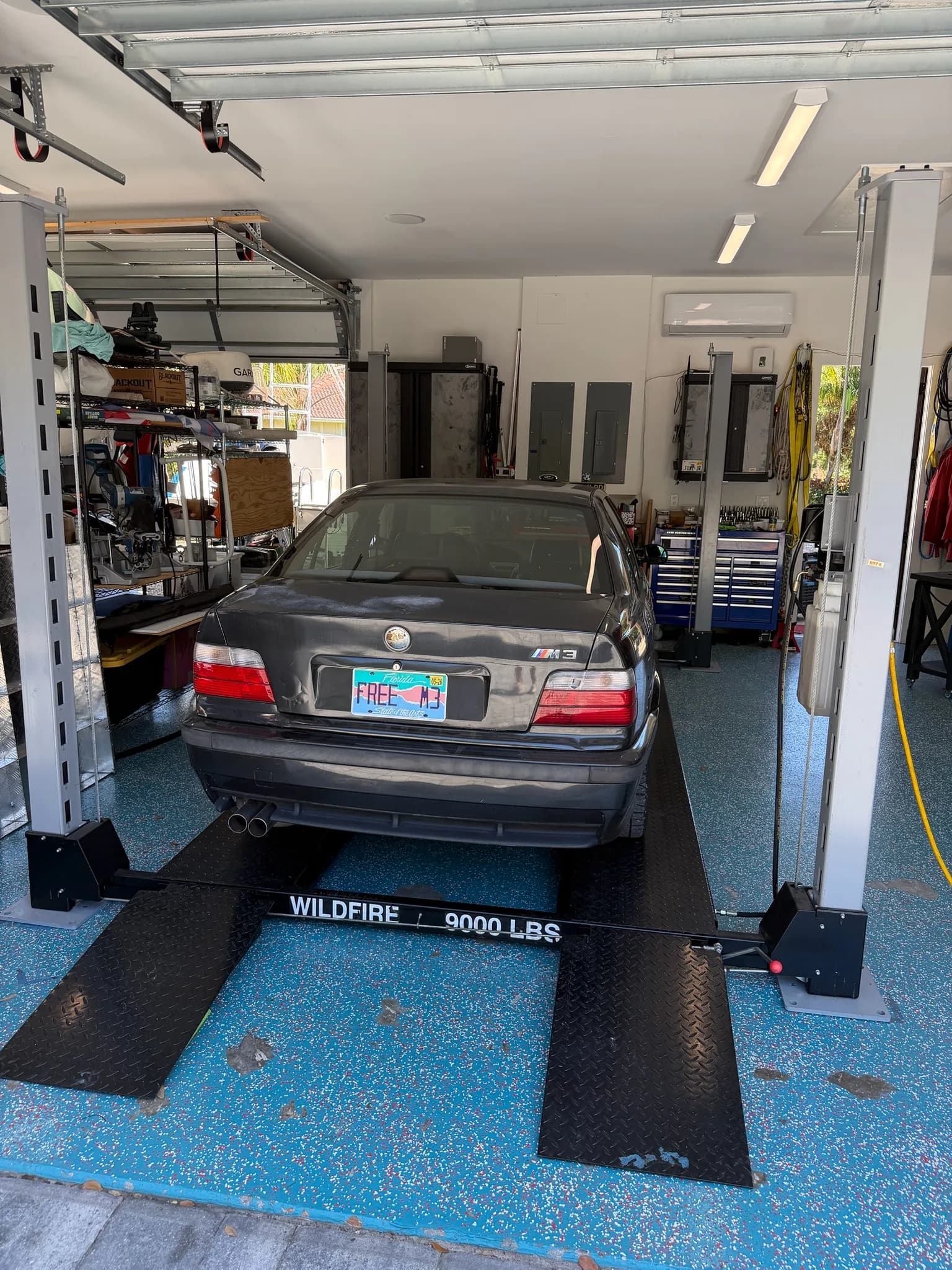 A black E36 BMW M3 raised on a four-post lift in the shop
