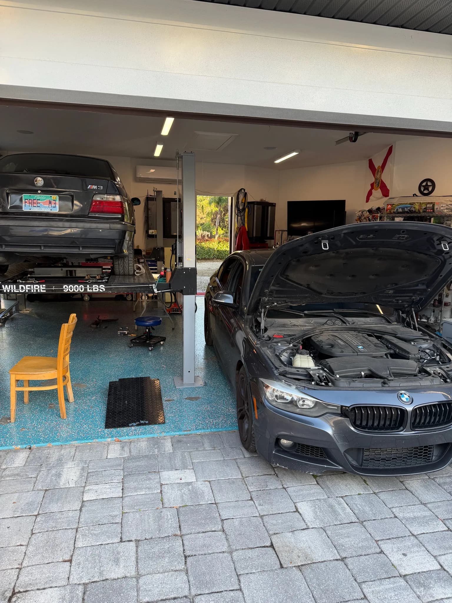 An E36 M3 on the lift beside a modern BMW 3-series with its hood open